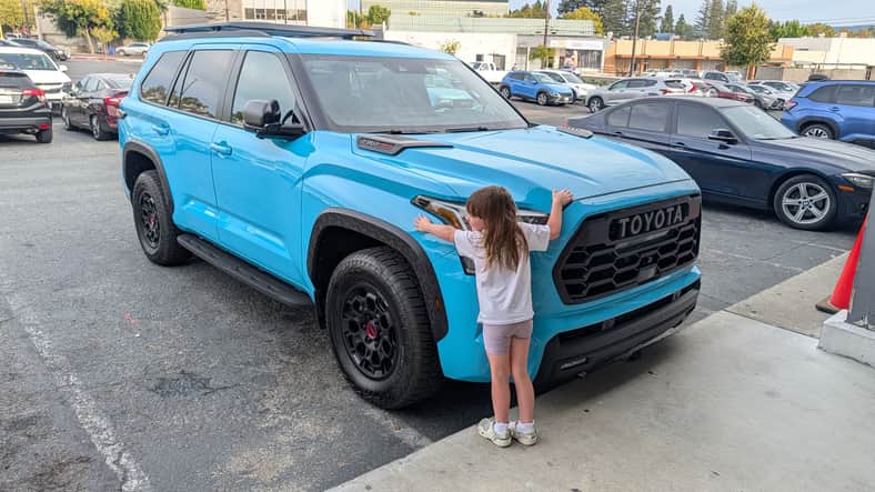 My daughter hugging a 2026 Toyota Sequoia in Wave Maker Blue